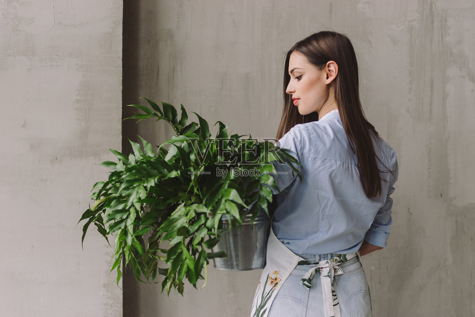 花店工作空间:年轻漂亮的白人妇女制作花卉装饰品，一束绿叶在她的手。照片摄影图片