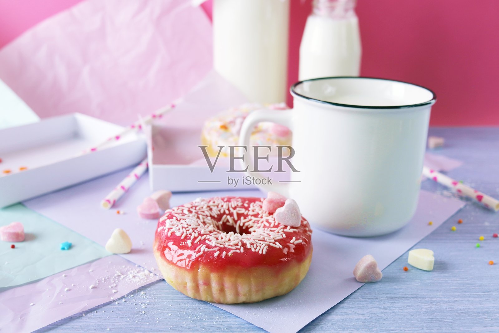 刚出炉的甜甜圈上了釉，撒上了焦糖心，牛奶和酸奶，装在杯子和玻璃瓶里，还有淡紫色的包装纸照片摄影图片