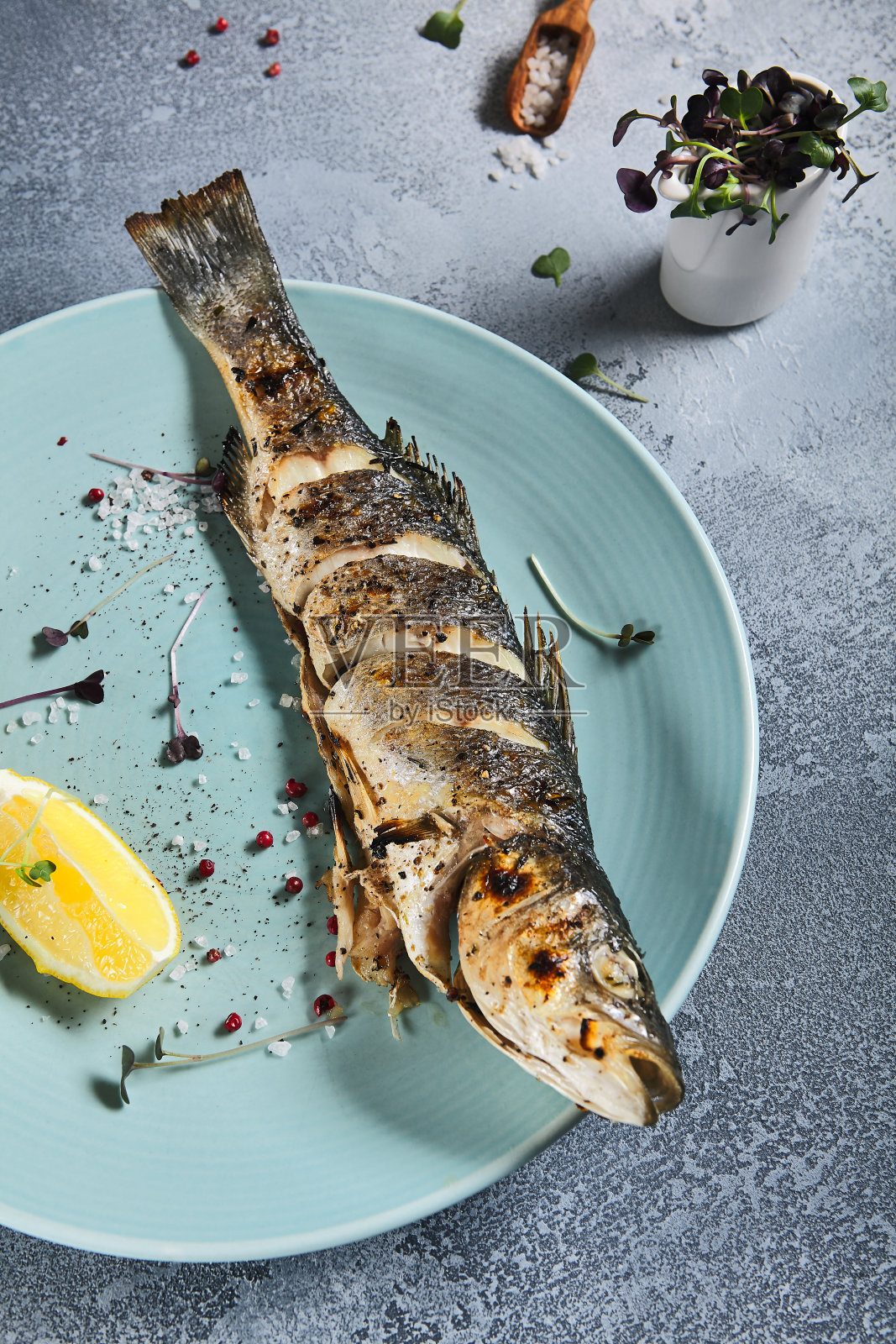 蓝色板烤鲈鱼，石材背景与纺织品。烤鱼在餐厅的菜单概念。柠檬烤虹鳟鱼。当代海鲜菜单。地中海食物。照片摄影图片