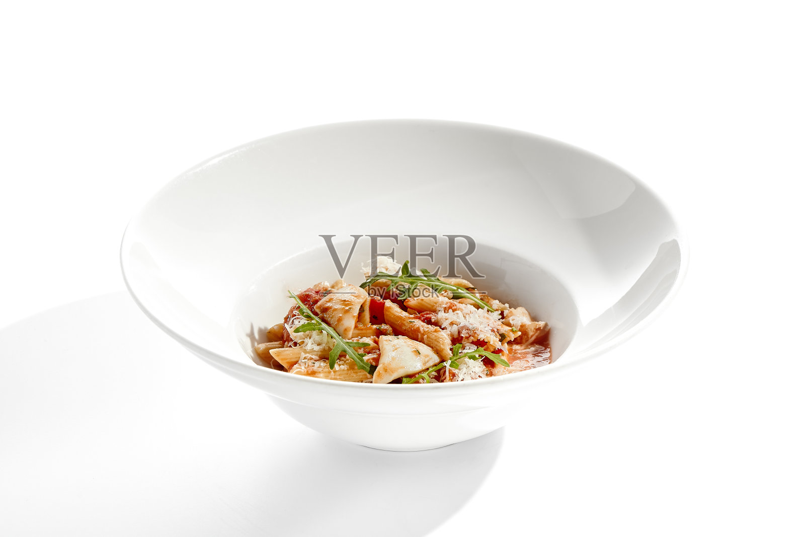 意大利传统菜肴——三文鱼通心粉、鱿鱼、番茄酱和橄榄。白色餐桌上有海鲜通心粉。意大利海鲜意面配arrabiata酱——健康的地中海午餐。照片摄影图片