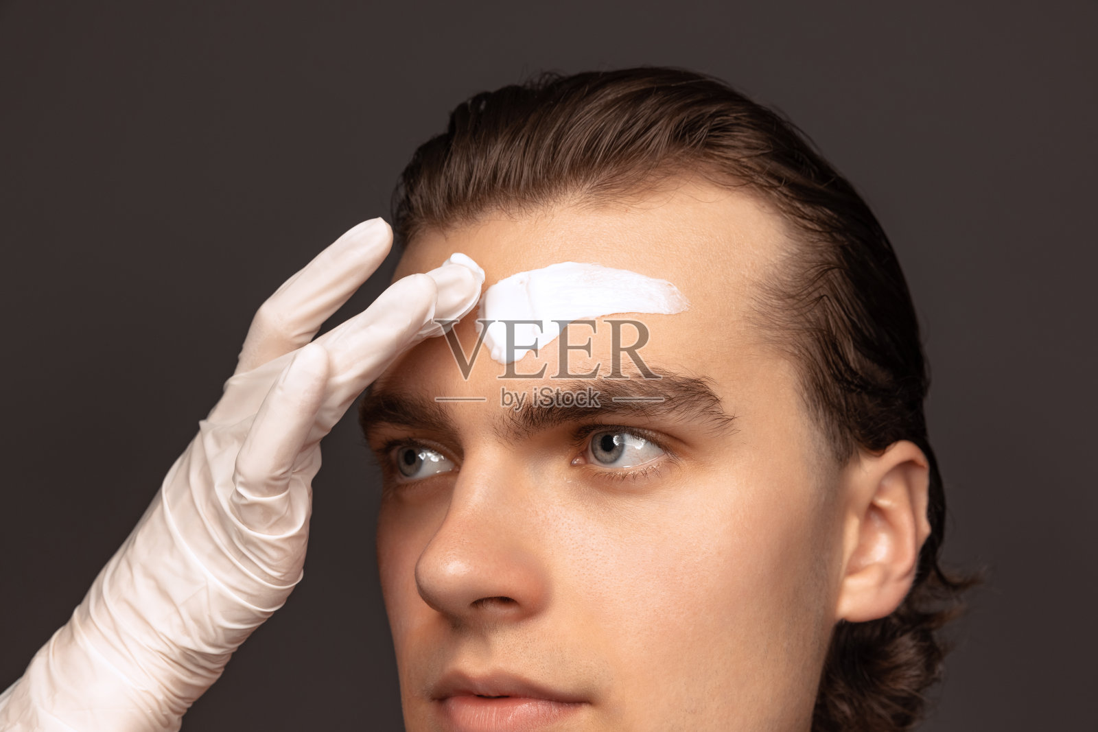 保湿面膜。一名男子用面霜面膜在灰色背景下保持完美的皮肤。化妆品、保健、护肤、美容照片摄影图片