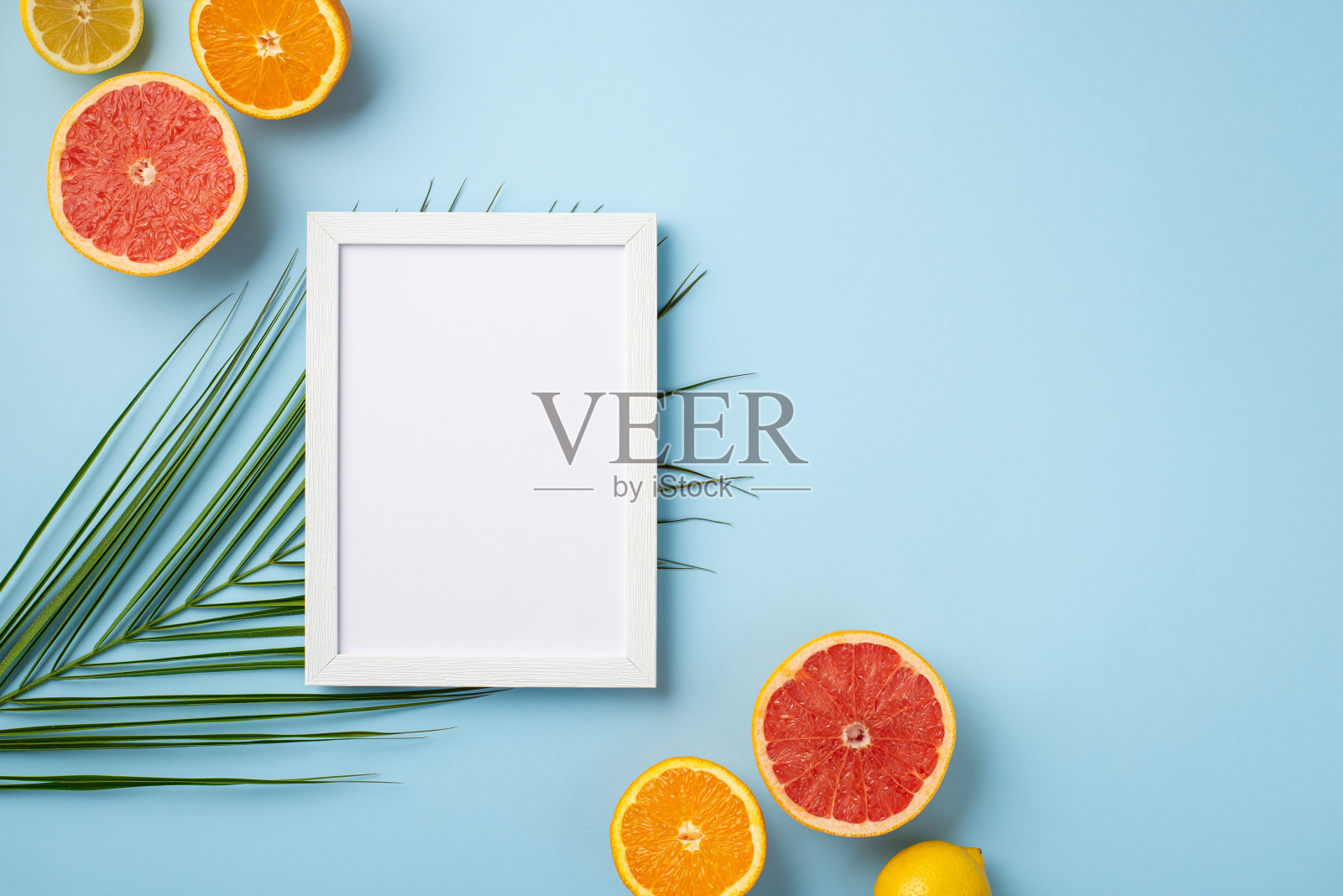 暑假的概念。俯视照片的白色相框和成熟的热带水果切柠檬橙子柚子和棕榈叶孤立粉彩蓝色背景与空白照片摄影图片