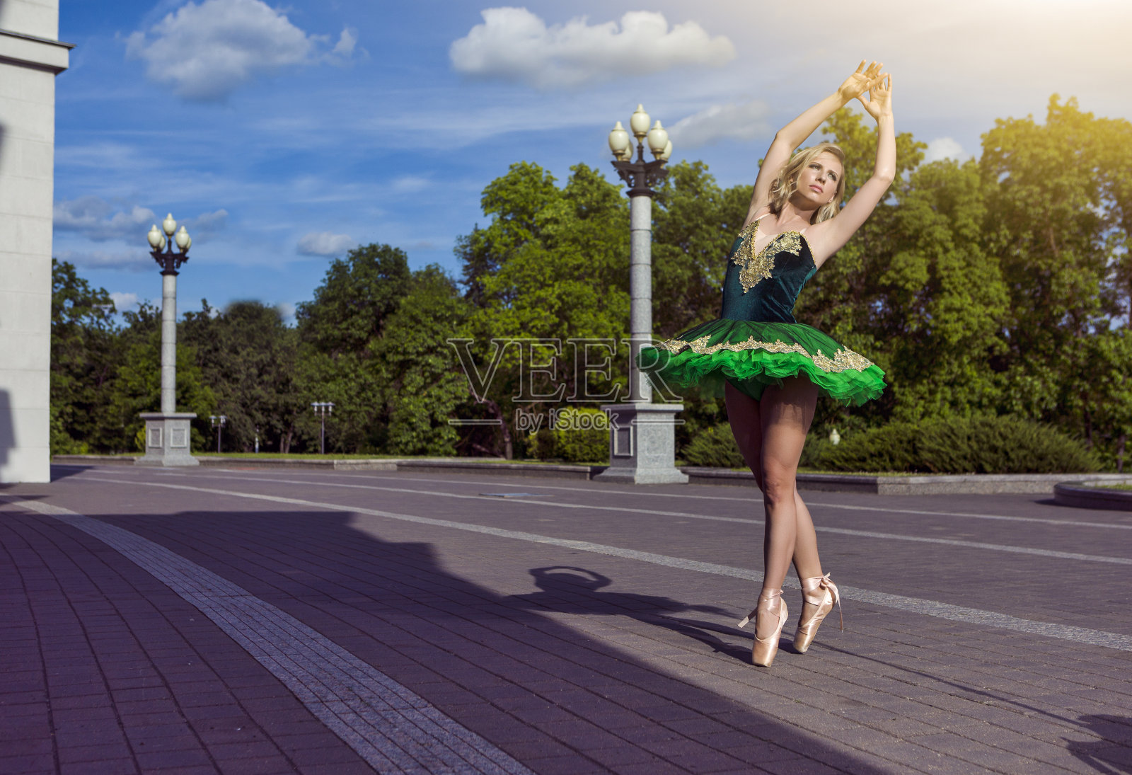 迷人的年轻专业白人芭蕾舞演员在绿色芭蕾舞裙摆在舞蹈姿势，而双手在户外举起照片摄影图片