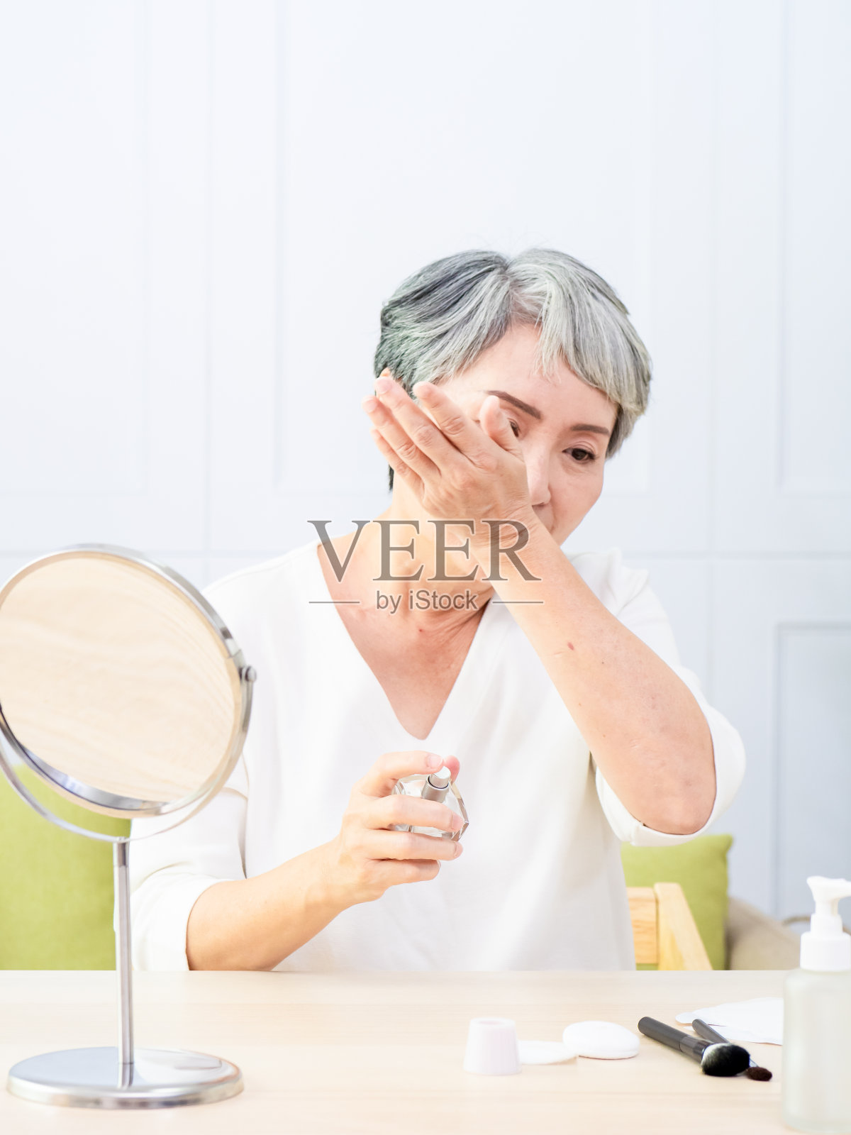 快乐的年老亚洲妇女应用乳液对她的脸。照片摄影图片