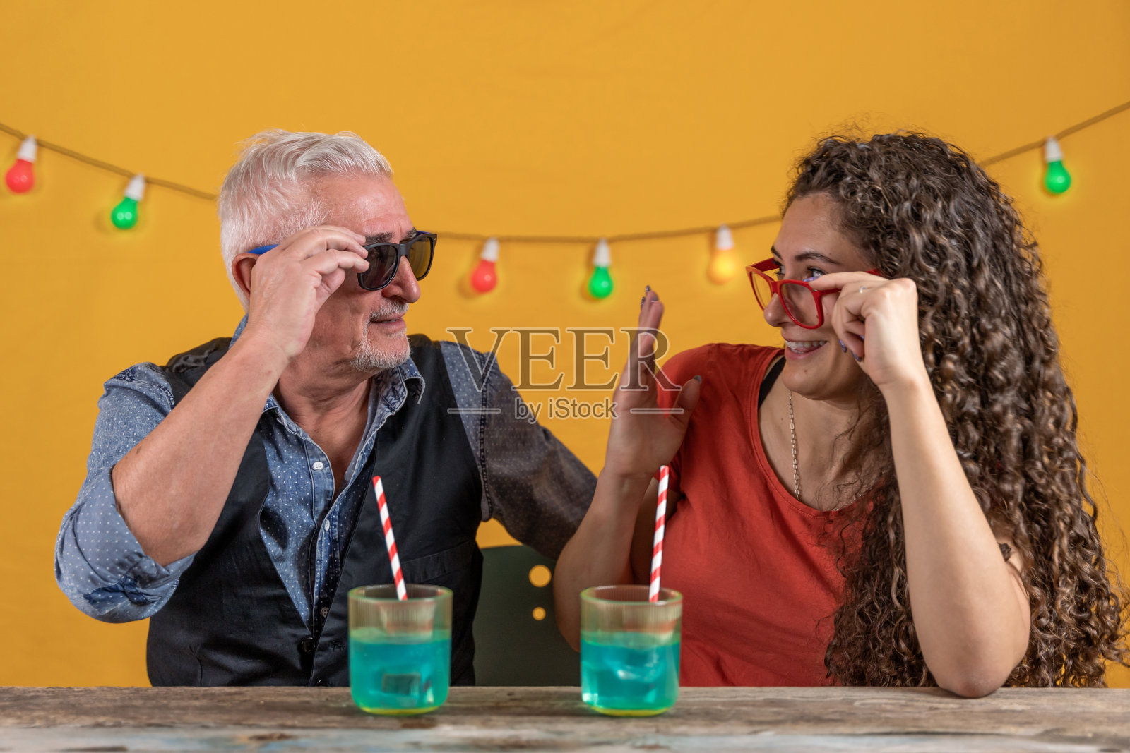 父亲和女儿坐在黄色背景下喝着蓝色鸡尾酒照片摄影图片