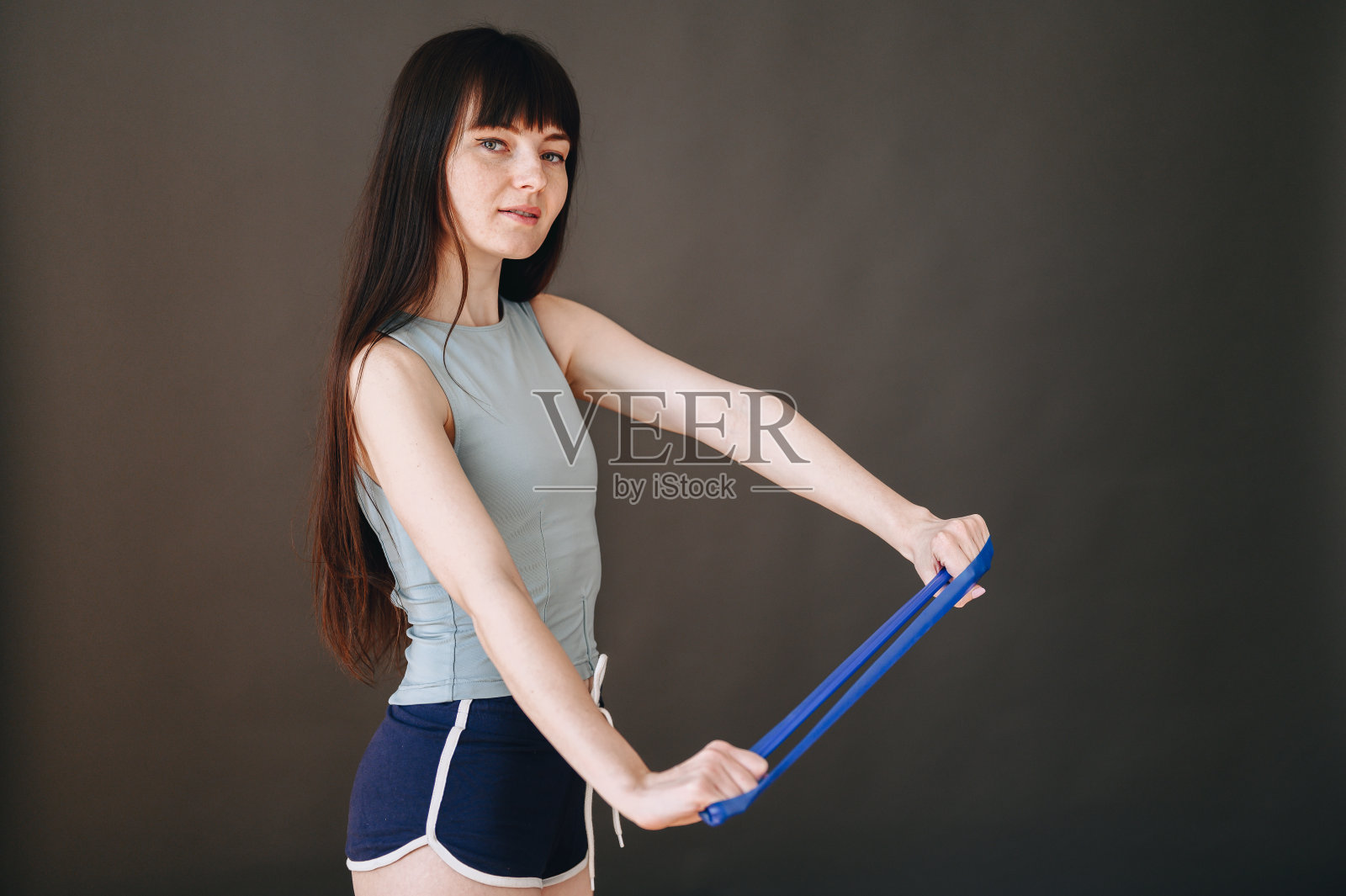 一个瘦弱的女孩在黑色的背景上用橡皮筋做手操。照片摄影图片