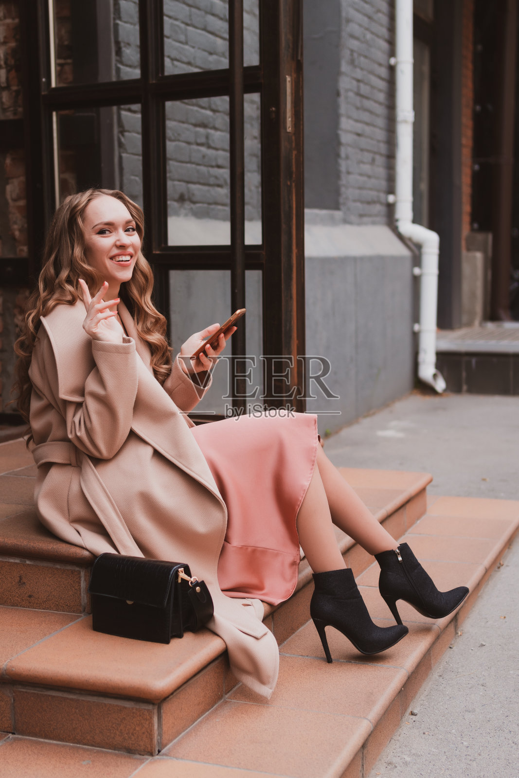 美丽的年轻女子穿着舒适的外套在城市里走来走去，坐在台阶上，用手机留言照片摄影图片