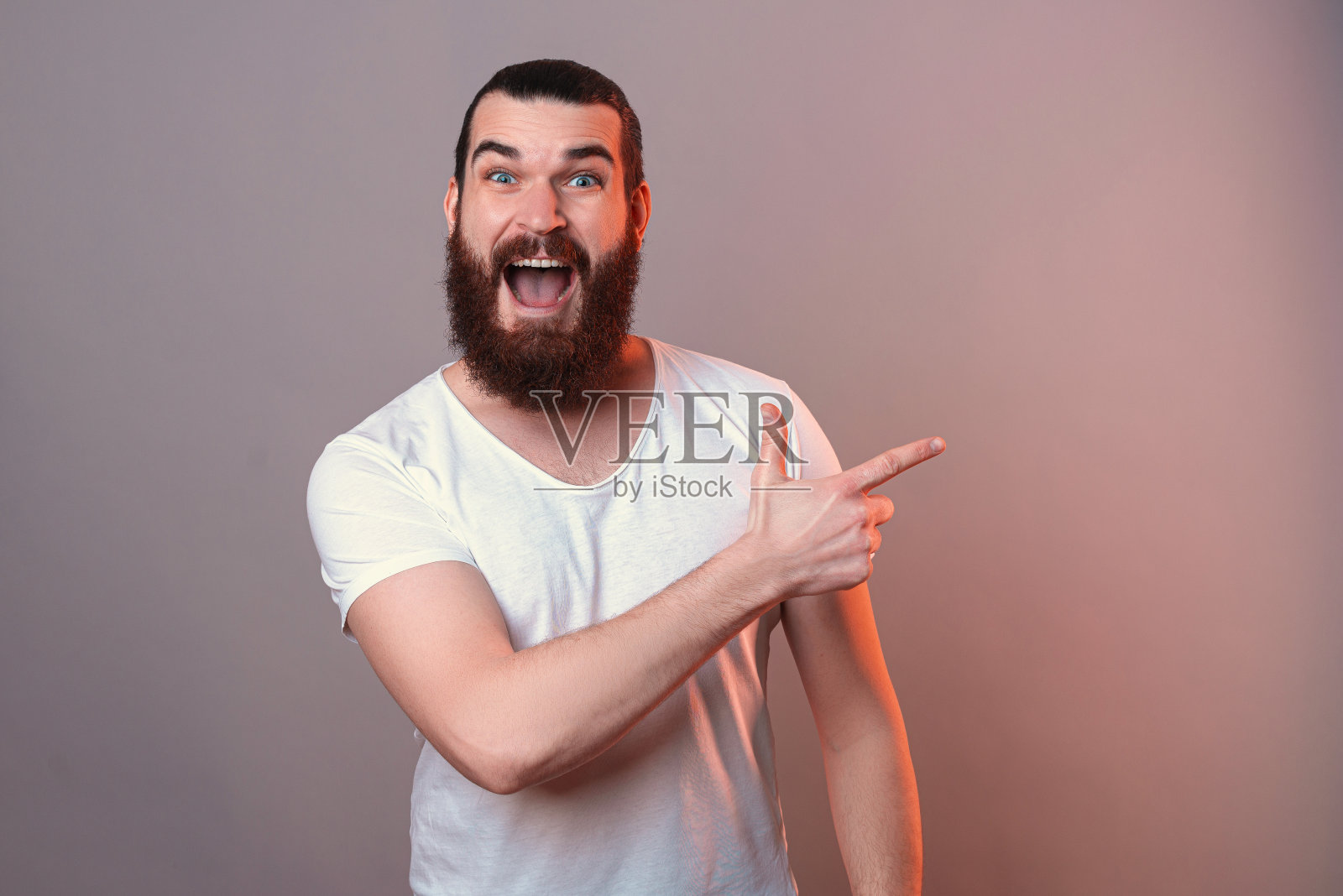 满脸胡须的男子欣喜若狂地指着一边看着镜头。照片摄影图片