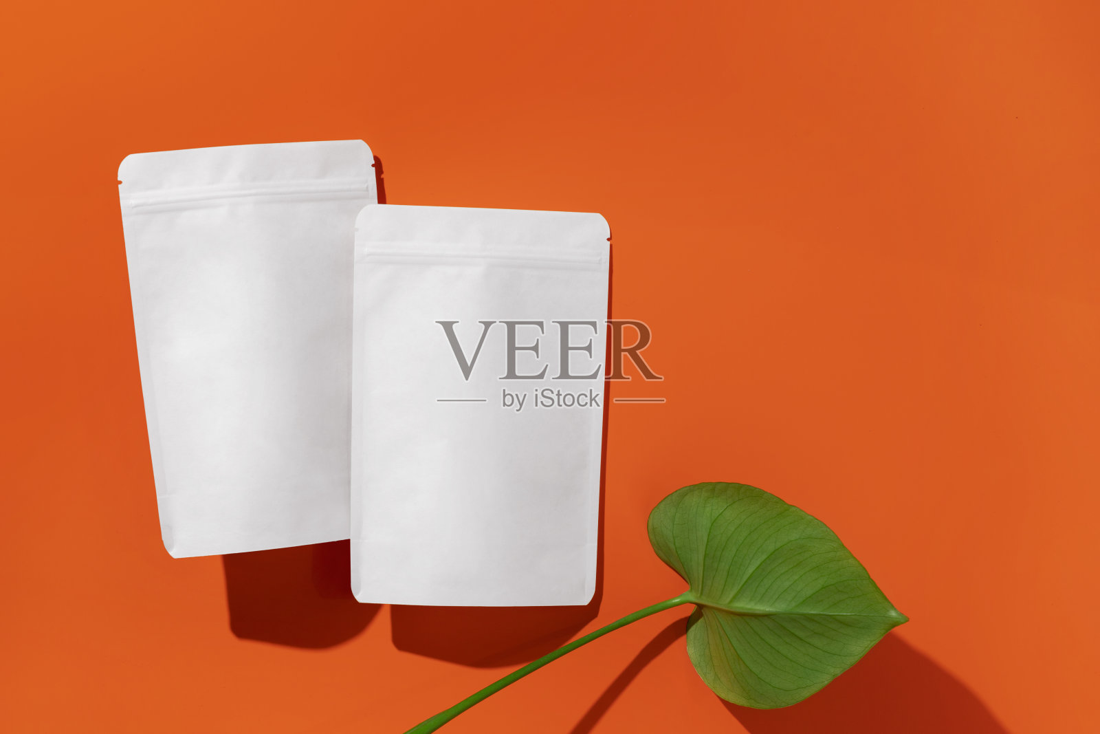 白色纸板包装的茶/咖啡/香料/小吃和monstera叶在橙色的背景。品牌和包装模型。照片摄影图片