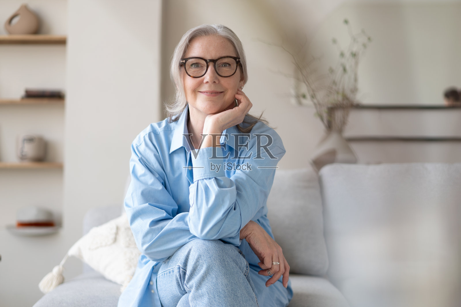 快乐成熟的女人在家里客厅的沙发上放松。老妇人看着镜头照片摄影图片