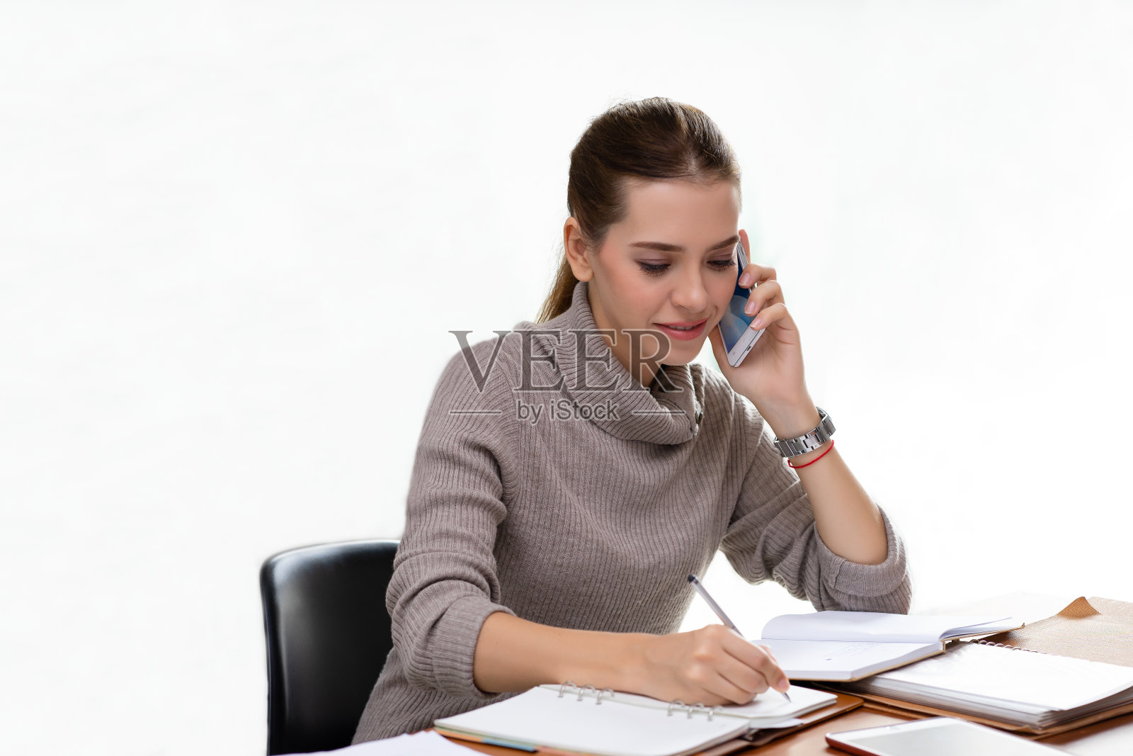 年轻的女商人在工作打电话和做笔记，坐在她的工作地点在白色孤立的背景。照片摄影图片