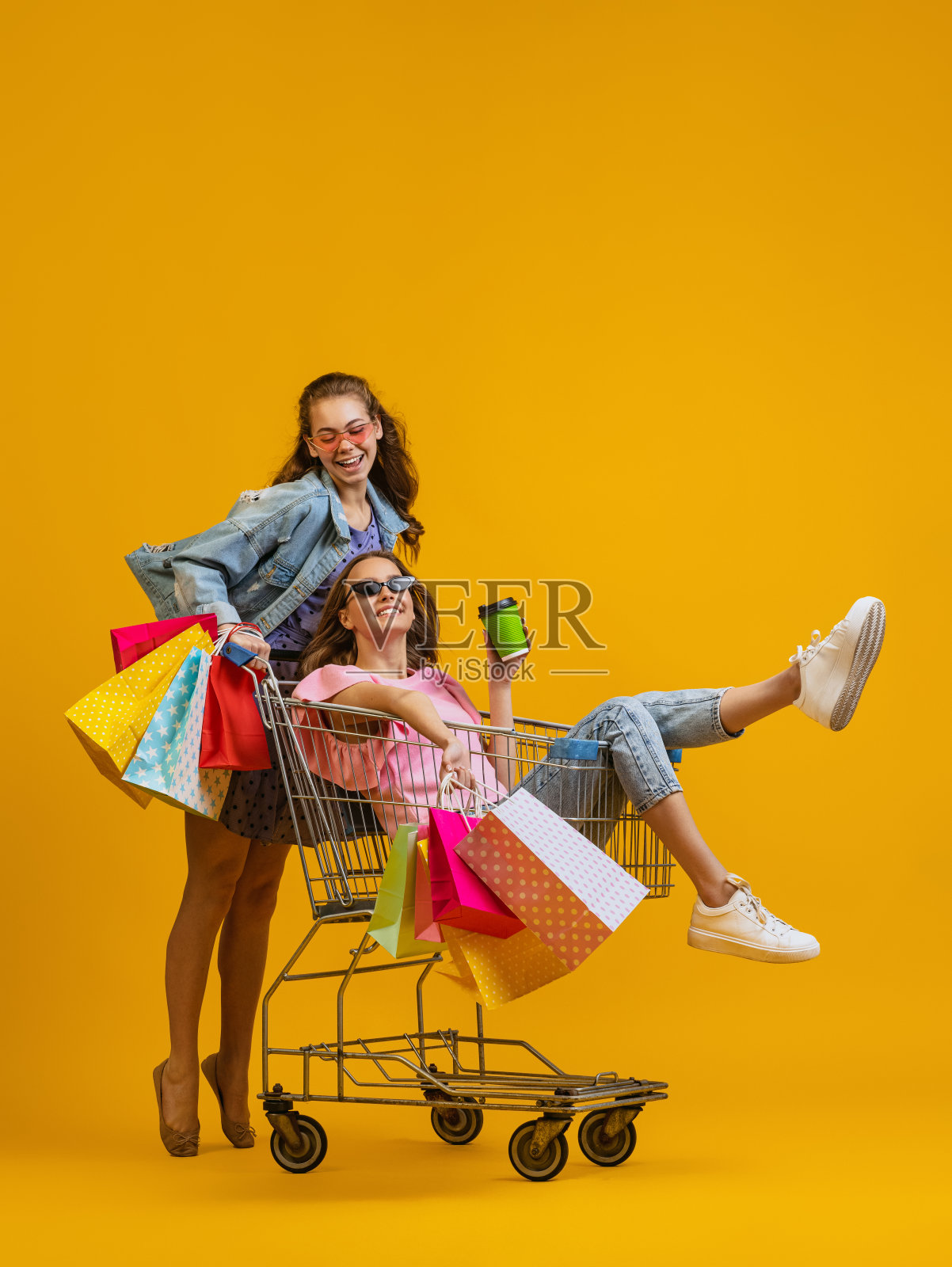 漂亮年轻惊讶的女孩去购物与购物车孤立在明亮的黄色背景。销售概念，黑色星期五，折扣，情绪照片摄影图片