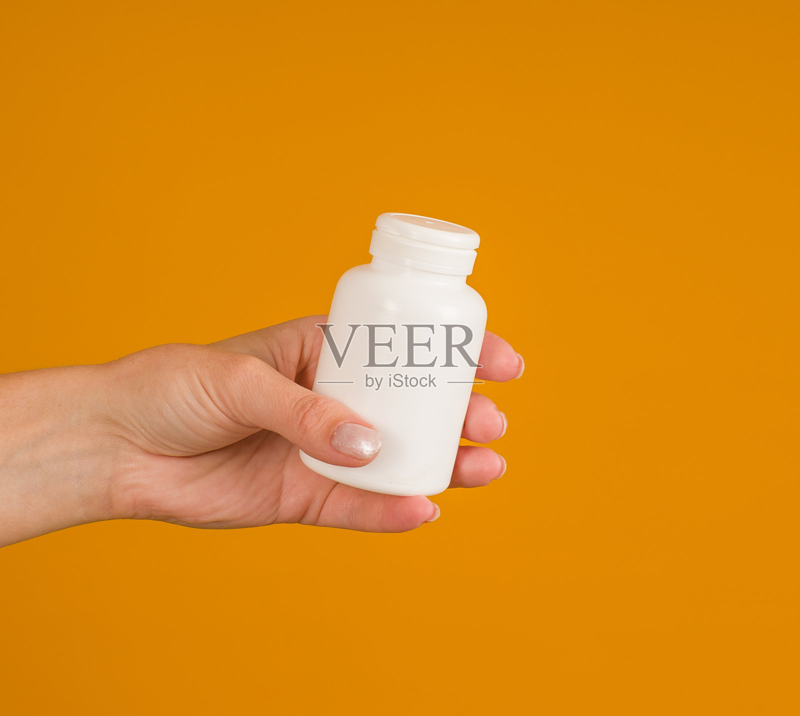 特写：手持黄色背景的白色药瓶照片摄影图片