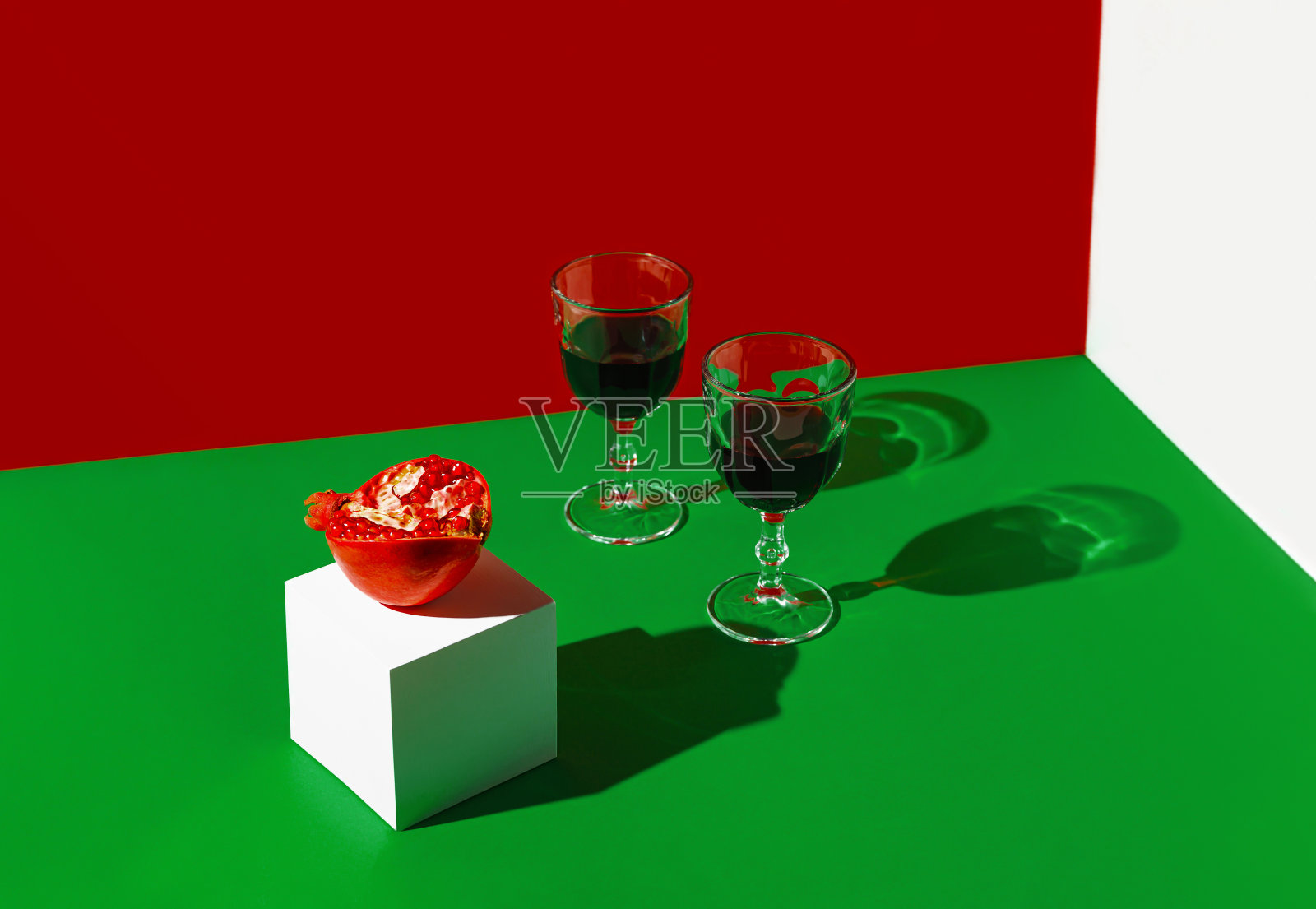 创作构成的玻璃红酒或果汁和石榴在绿色的背景下与阳光和阴影。夏季饮料的概念。最小的风格。照片摄影图片