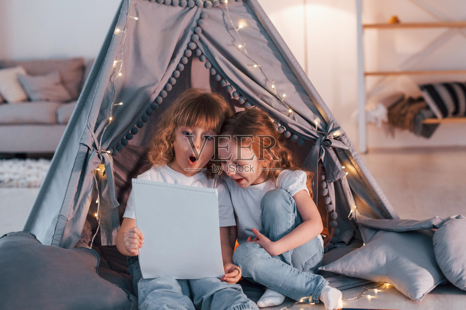 好奇地拿着写有信息或艺术的纸。两个小女孩一起在家庭房间的帐篷里照片摄影图片