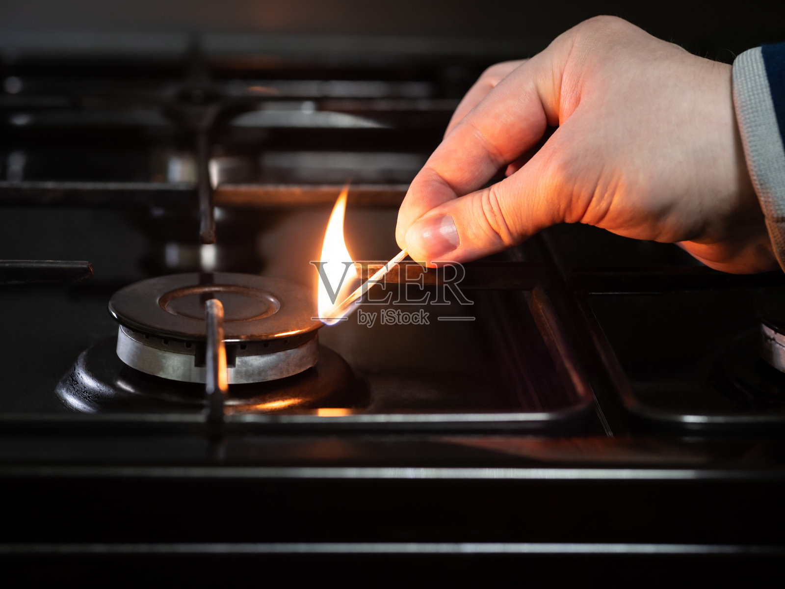 一个男人用一根燃烧的火柴点燃了煤气炉。煤气炉燃烧器。照片摄影图片