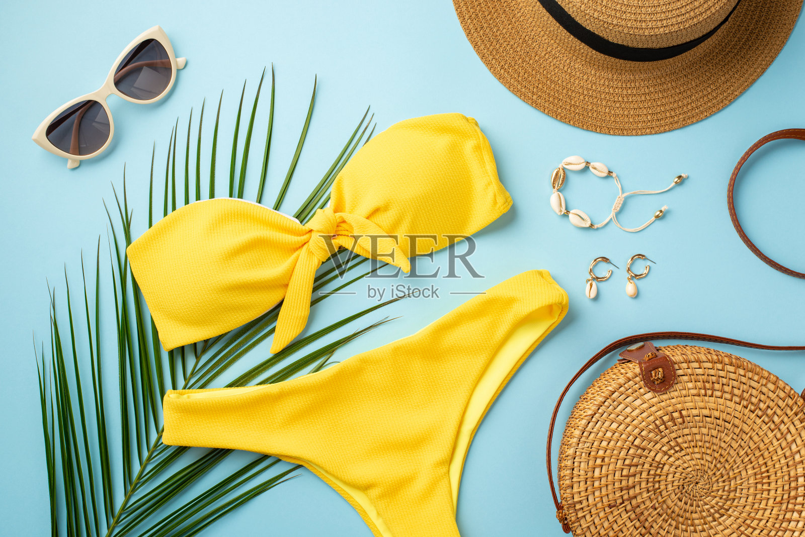 暑假的概念。顶视图照片的帽子贝壳手镯耳环时尚太阳镜黄色比基尼圆藤包和棕榈叶在孤立粉彩蓝色背景照片摄影图片