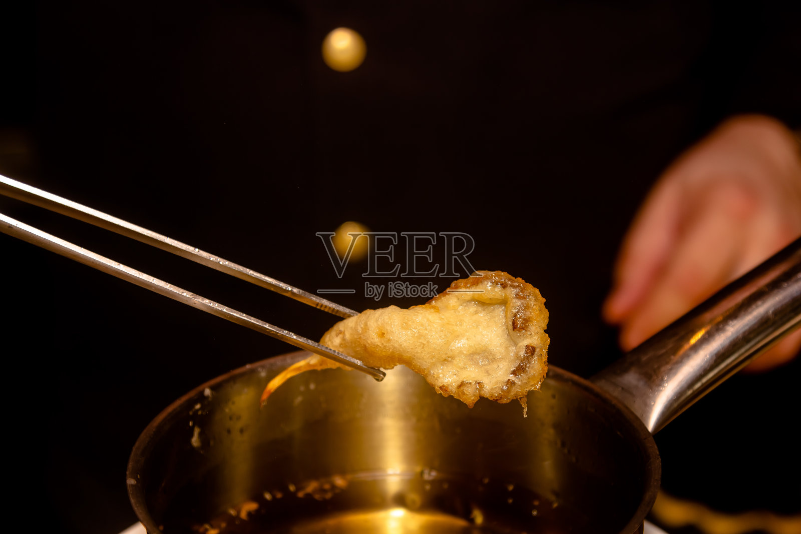 用油锅煎天妇罗虾。拿一个煎好的大虾。照片摄影图片