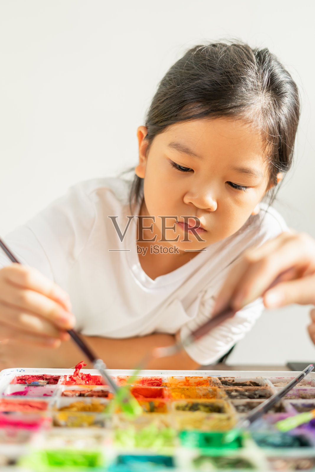 可爱的小朋友穿着白衬衫，看颜色，拿着画笔，在教育教室里选择混合颜色。亚洲美丽的孩子们快乐而有趣的彩绘教育在小学校照片摄影图片
