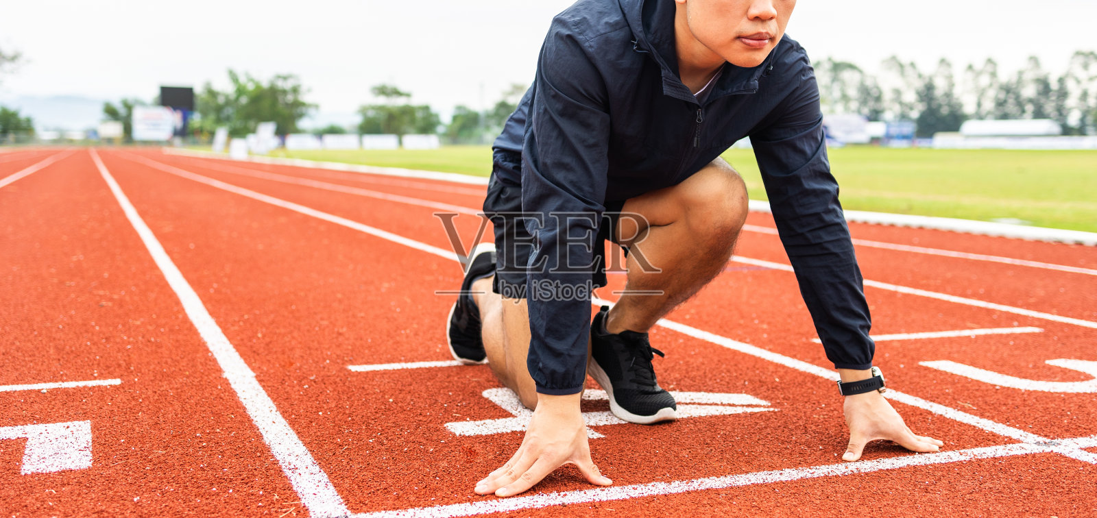 年轻英俊的中国男子在体育场跑道上跑步锻炼前摆明星姿势。挑战运动员在起跑点奔跑的比赛照片摄影图片