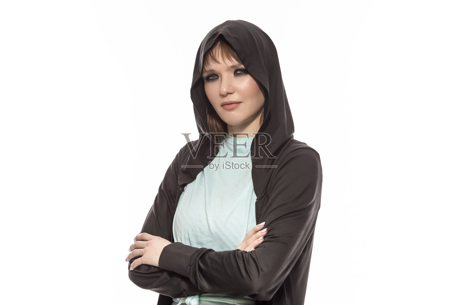 自然特写微笑迷人的金发白人女运动员在黑色帽衫与交叉的手摆姿势，而看着纯白色。照片摄影图片