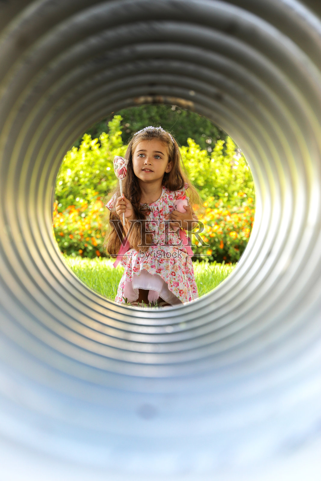 一个漂亮的女孩，棕色的头发，淡绿色的眼睛，穿着花裙，开心地笑着，拿着棒棒糖。照片摄影图片