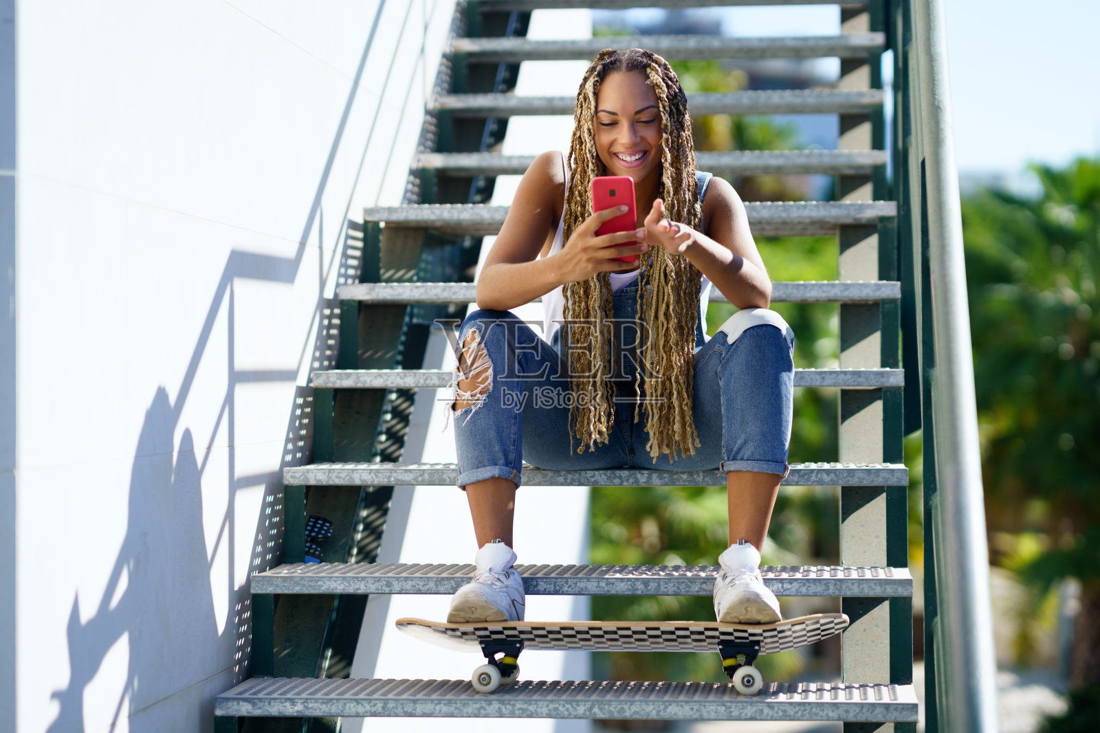 欢快的黑人女性滑板浏览智能手机在城市照片摄影图片