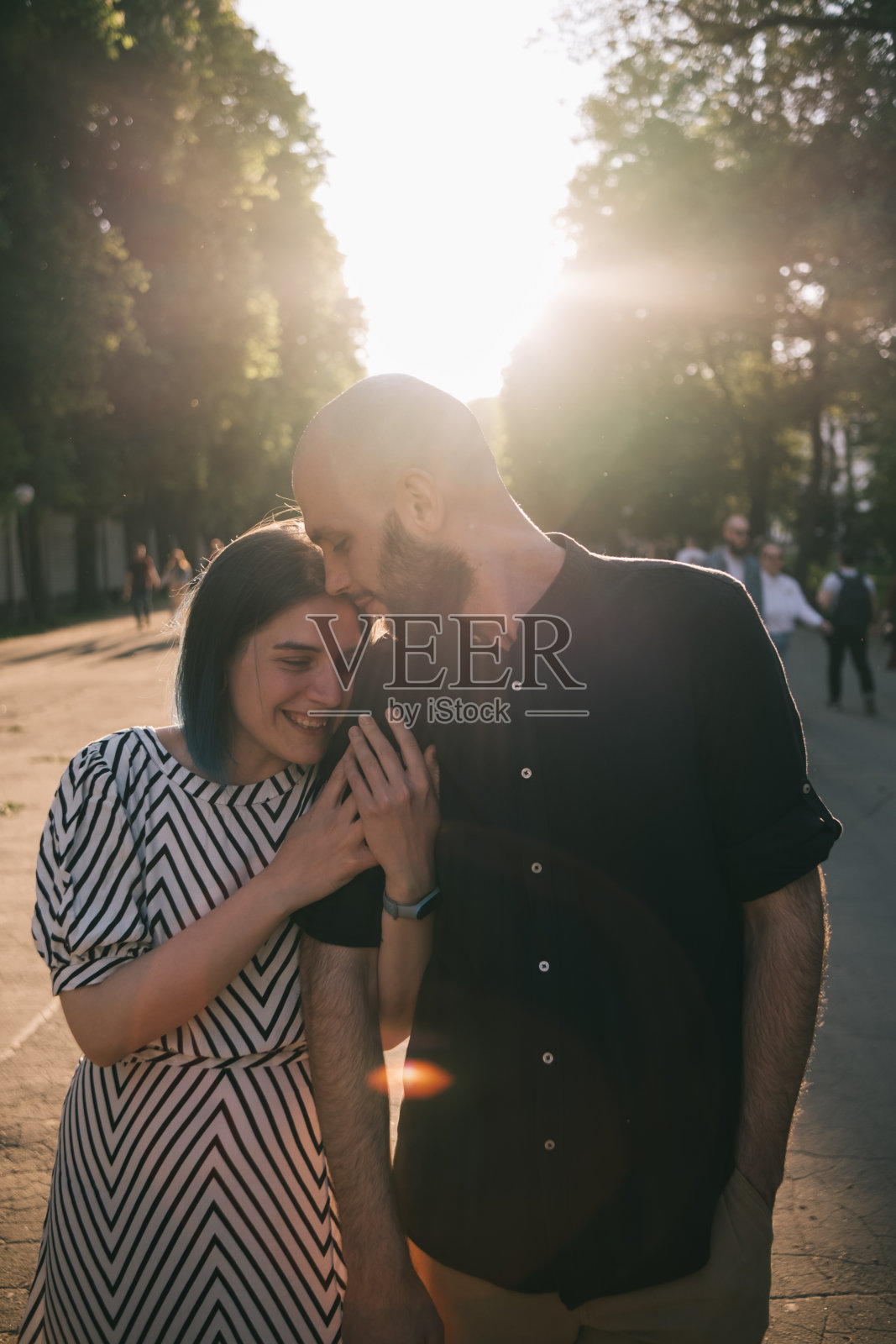 情侣们在夏天的公园里散步。女孩紧紧地握着男孩的手。耀眼的阳光照片摄影图片