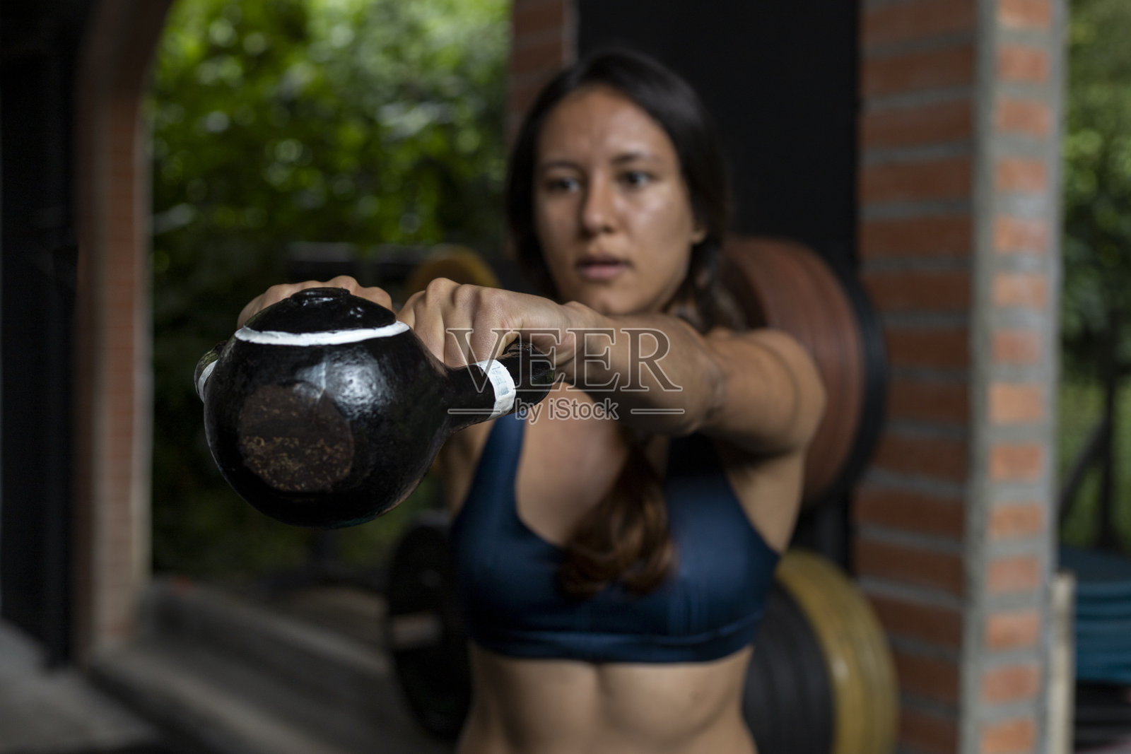一名拉丁美洲妇女在健身房进行高强度的功能性锻炼时，用双手举起壶铃。健康的生活方式概念。照片摄影图片