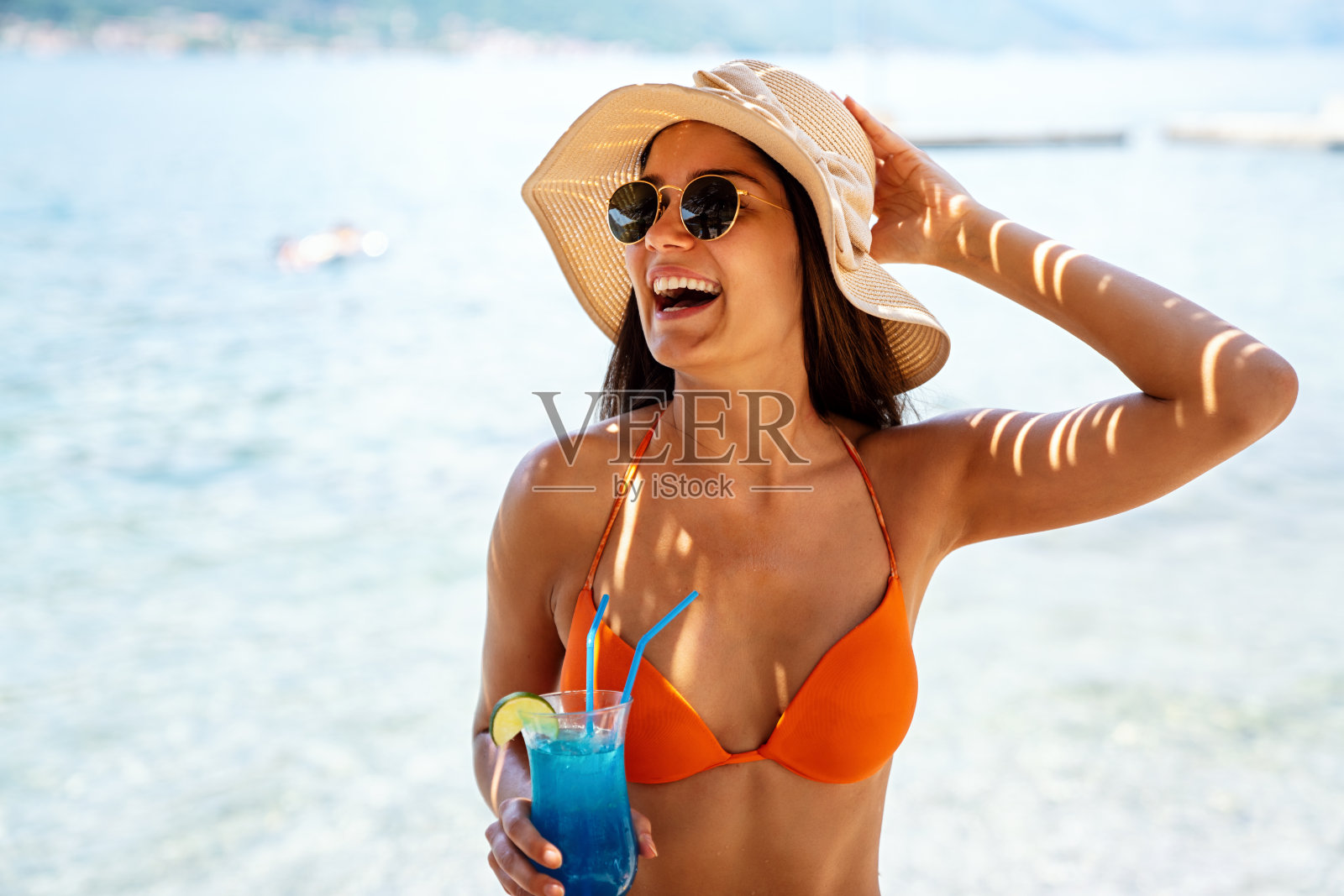 快乐的年轻女子穿着比基尼，享受鸡尾酒在暑假。照片摄影图片