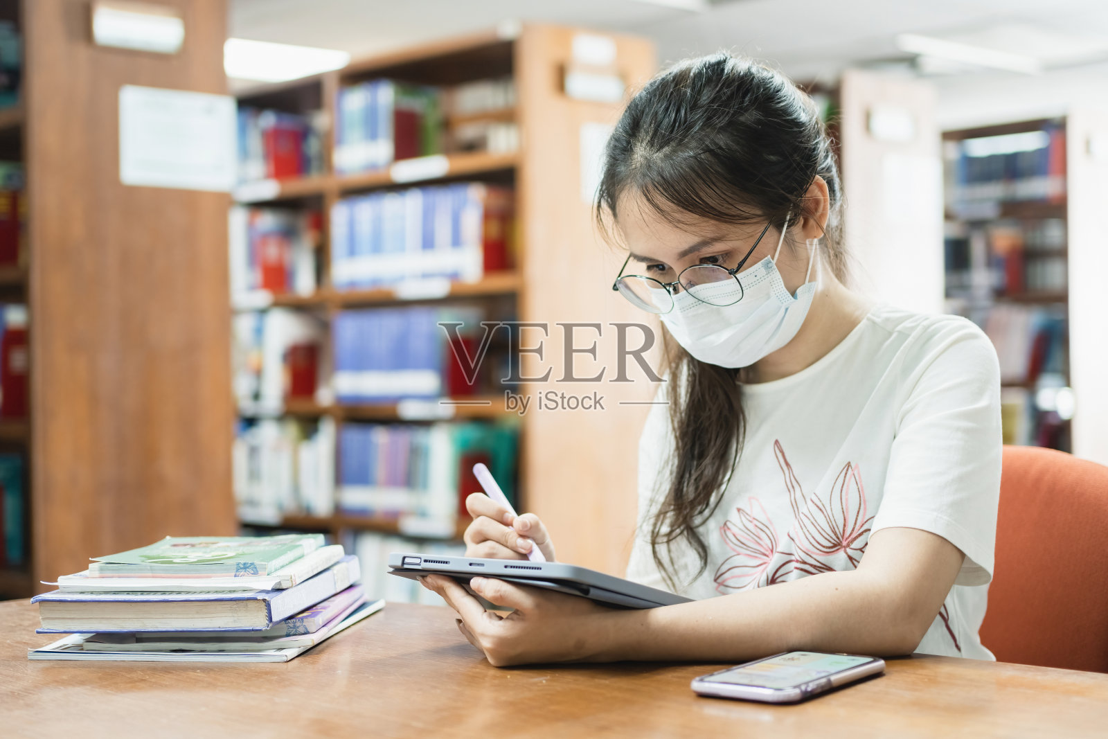 在图书馆里，一名亚洲女性用平板电脑和一本书搜索信息。照片摄影图片