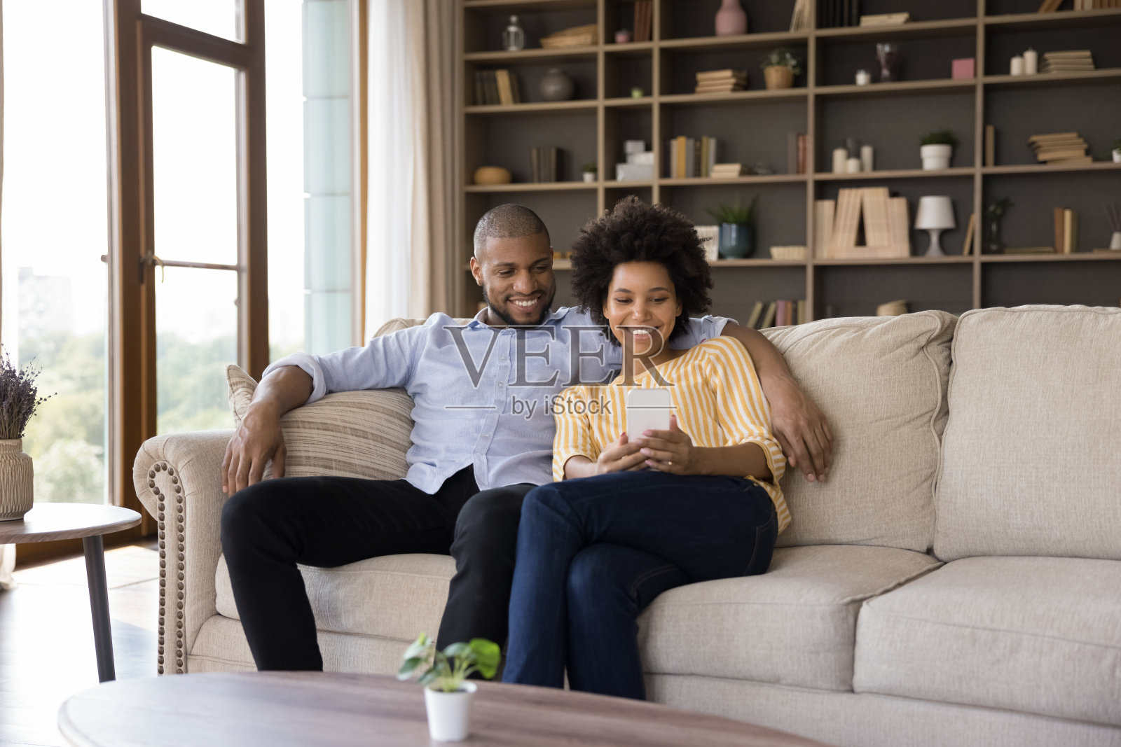 幸福的非洲夫妇坐在沙发上玩手机照片摄影图片