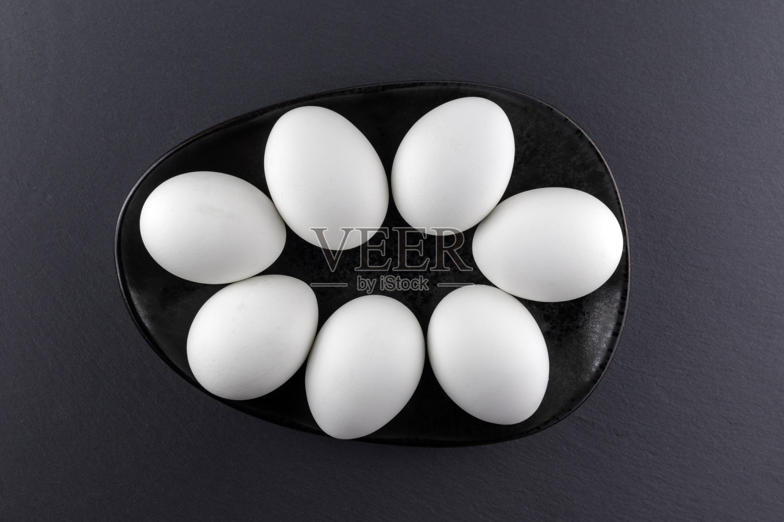 黑色背景上黑色盘子里的白色鸡蛋。前视图。照片摄影图片