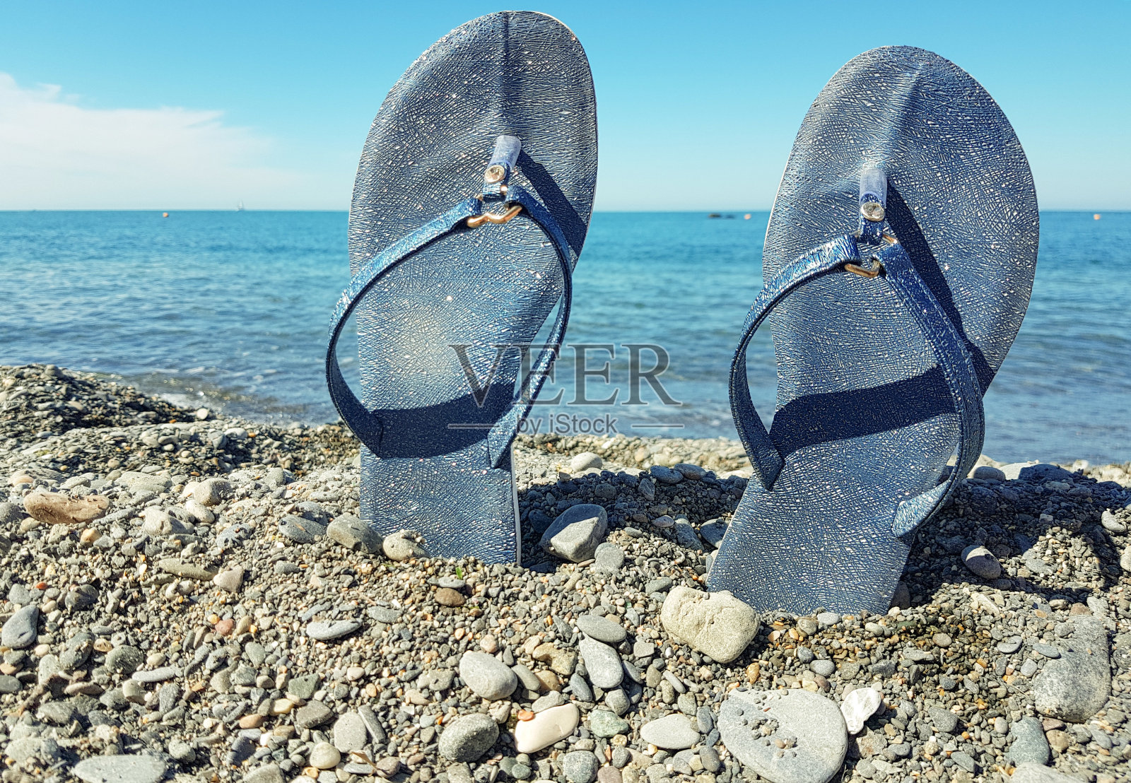 蓝色女子沙滩鞋，站在鹅卵石上，映衬着大海和蓝天。特写镜头，发短信的地方，海边海滩度假的概念照片摄影图片