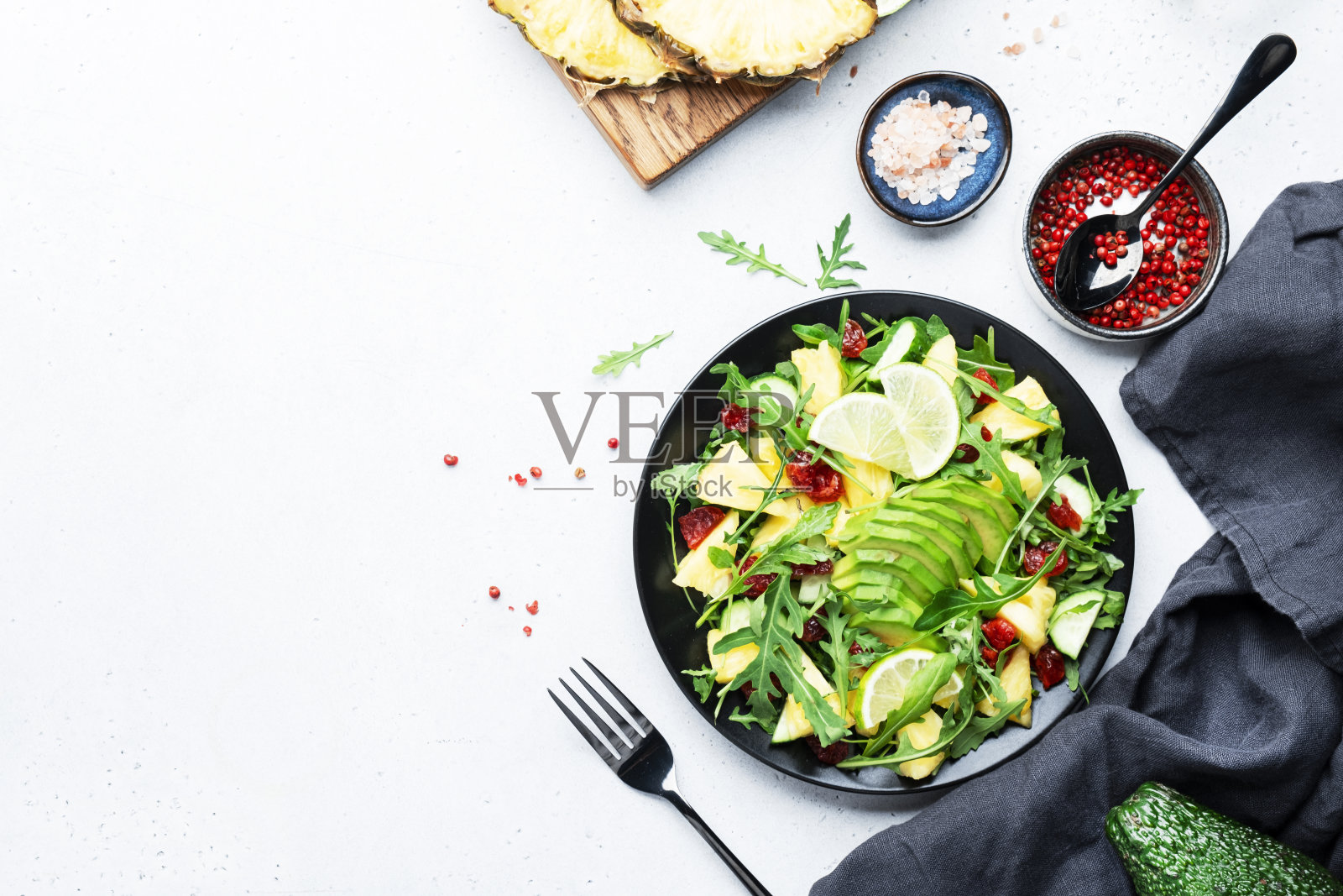 夏季素食沙拉，多汁菠萝，新鲜芝麻菜，鳄梨和干蔓越莓在白色的石头厨房桌子上，俯视图。健康饮食，清洁饮食，减肥理念照片摄影图片