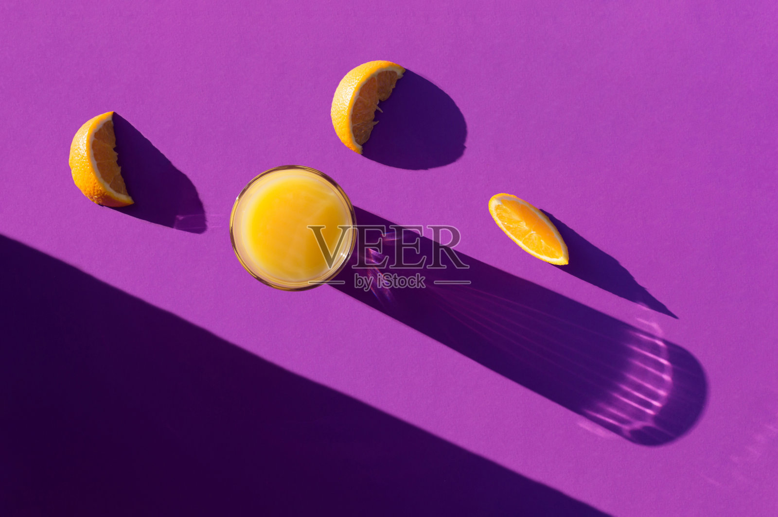 橙汁和橙片在深紫色的背景上有长长的阴影。照片摄影图片