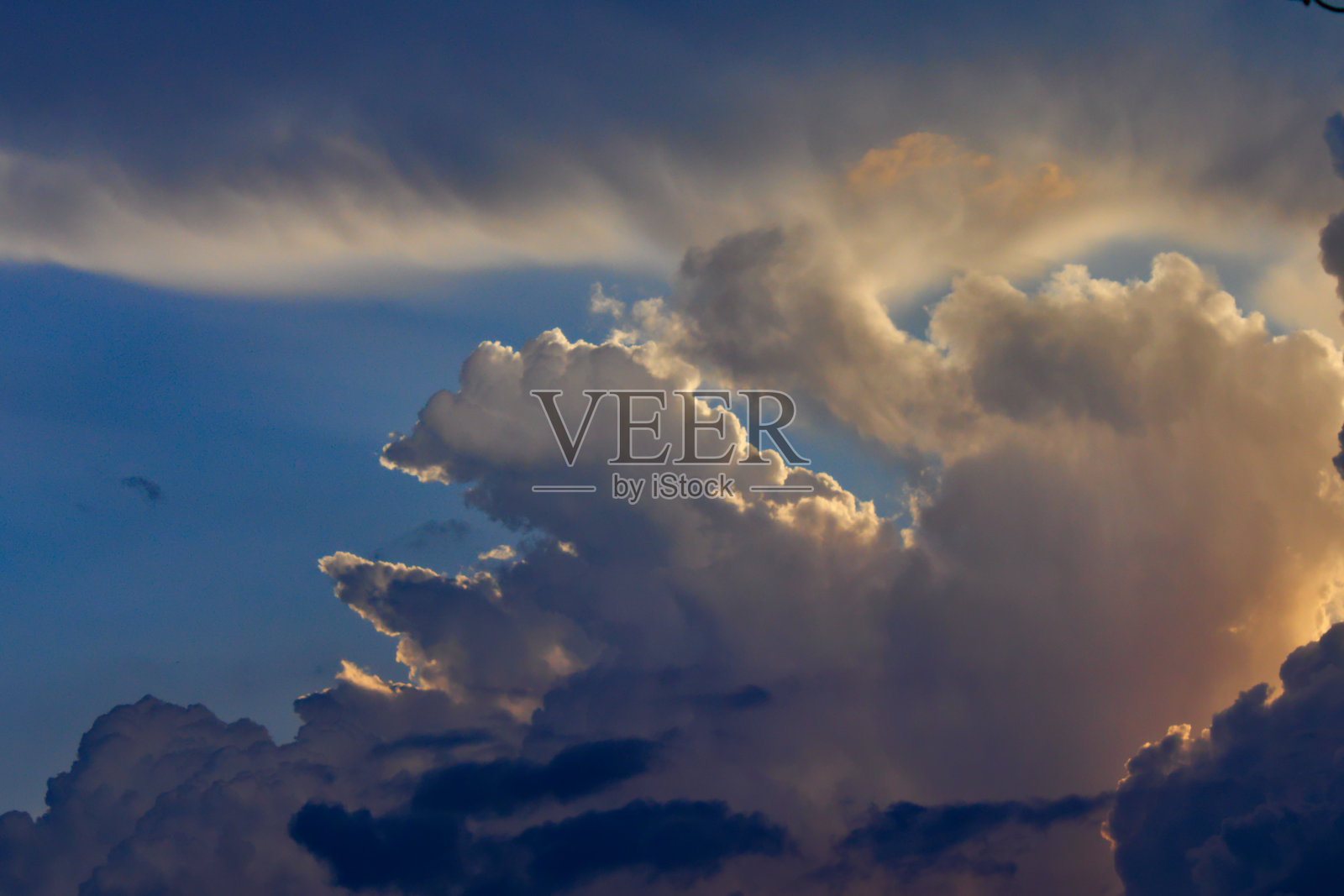 蓝色的天空，巨大的橘黄色积云和黑色的底部上升到地平线。照片摄影图片