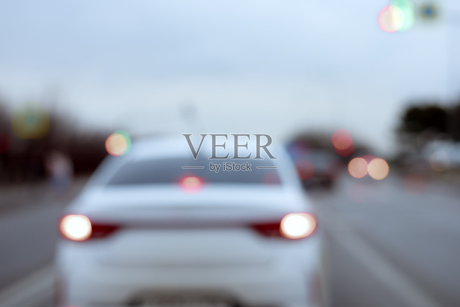 一辆开着前灯的白色汽车在多云的天气里行驶在路上。模糊的照片照片摄影图片