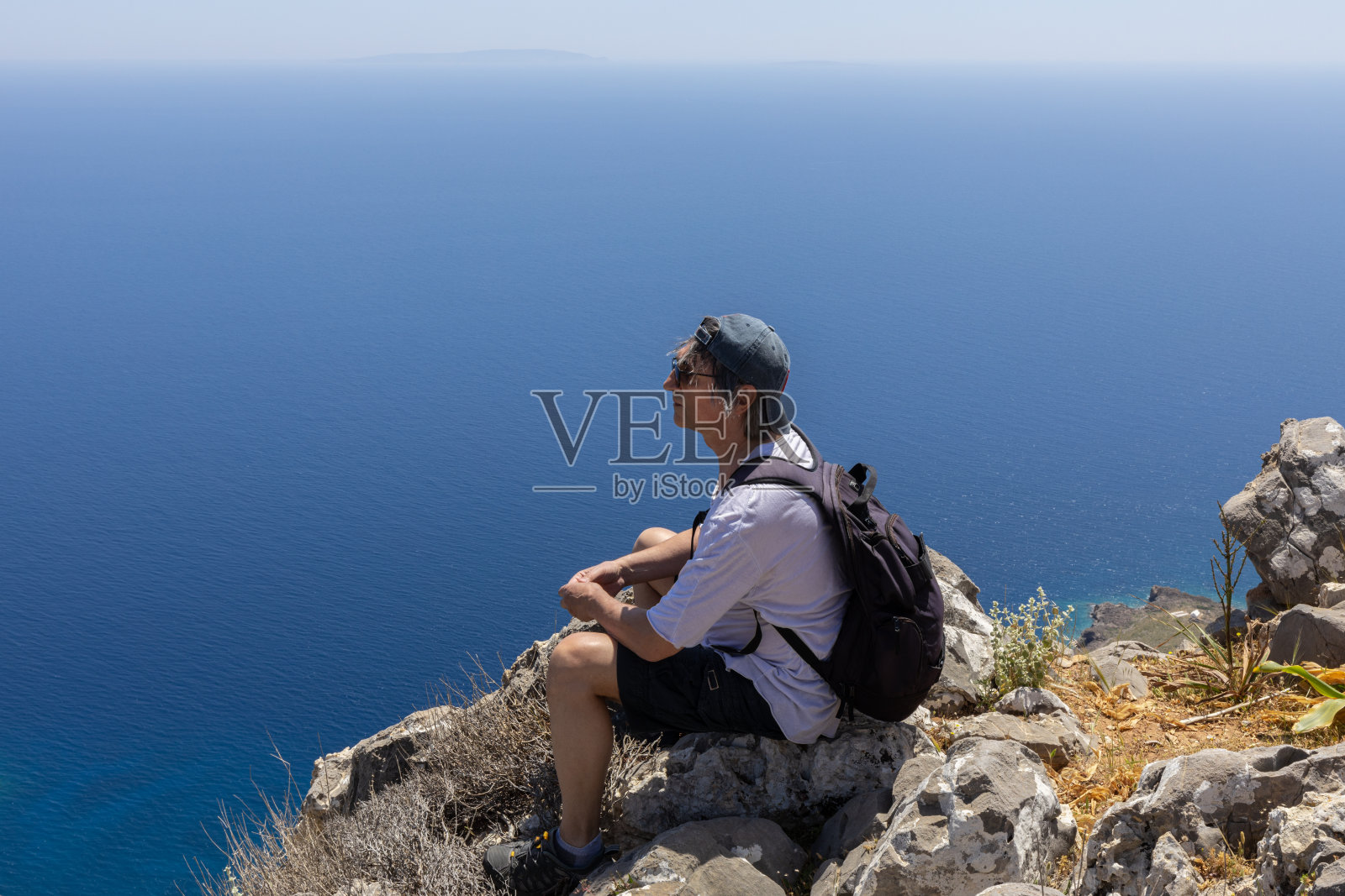 一个男人坐在海边的岩石上欣赏海景。积极的生活方式的概念。希腊克里特岛照片摄影图片