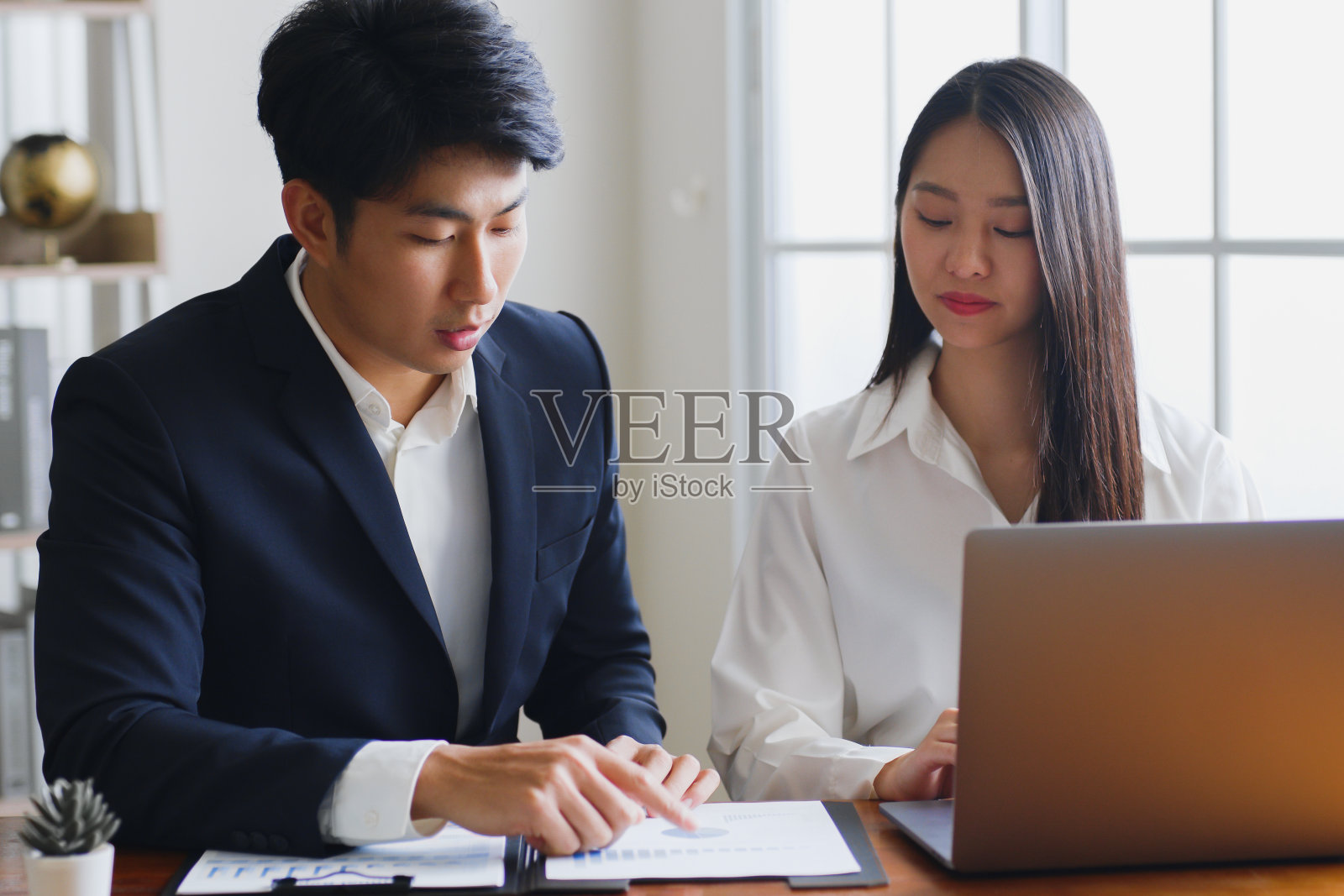 商人和年轻的亚洲女同事两人在办公室见面聊天。分享想法，讨论和指导笔记本电脑上的商业计划。照片摄影图片