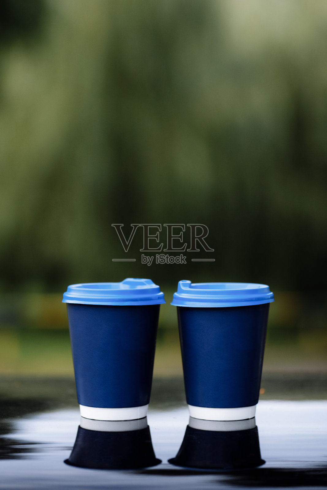 两个蓝色的纸咖啡杯在车顶上。在自然背景的黑色镜子上放着热茶的纸杯照片摄影图片