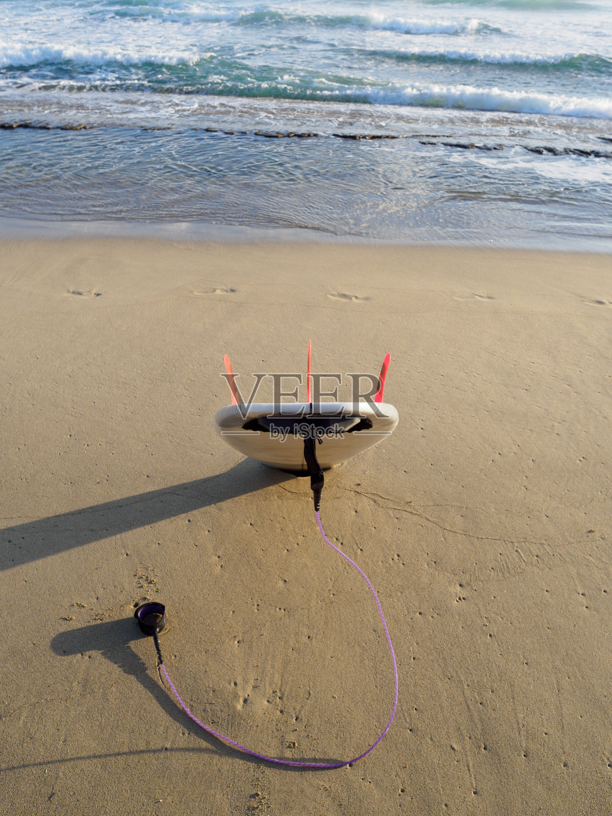 白色短冲浪板与紫色皮带在沙子准备冲浪。照片摄影图片