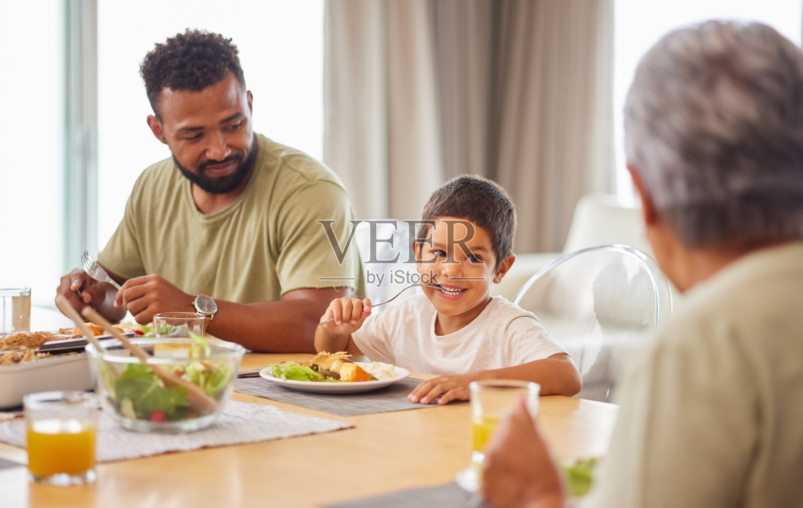 混血男人和儿子在休息室的餐桌旁享用午餐特写。西班牙裔父亲在家和儿子一起微笑用餐照片摄影图片