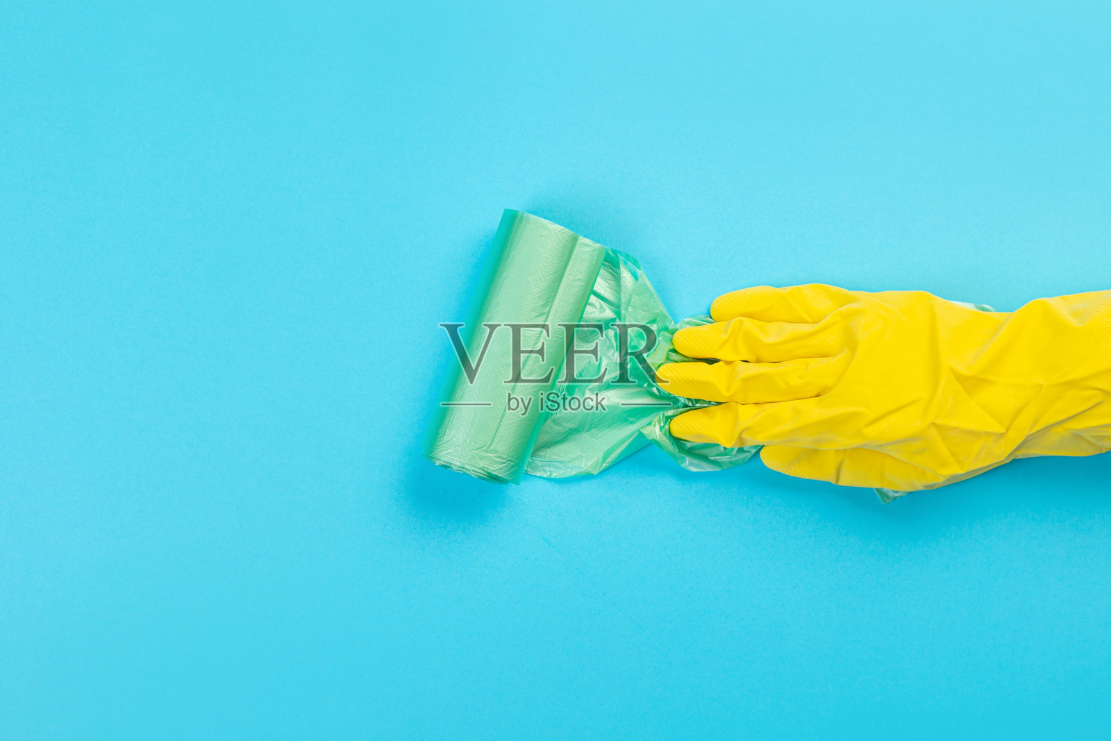 一只戴着黄色手套的手拿着蓝色背景的一次性塑料垃圾袋。放置与复制空间。照片摄影图片