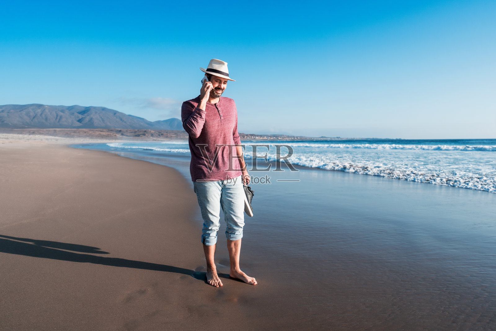 男人在日落时分的海滩上愉快地讲着手机照片摄影图片