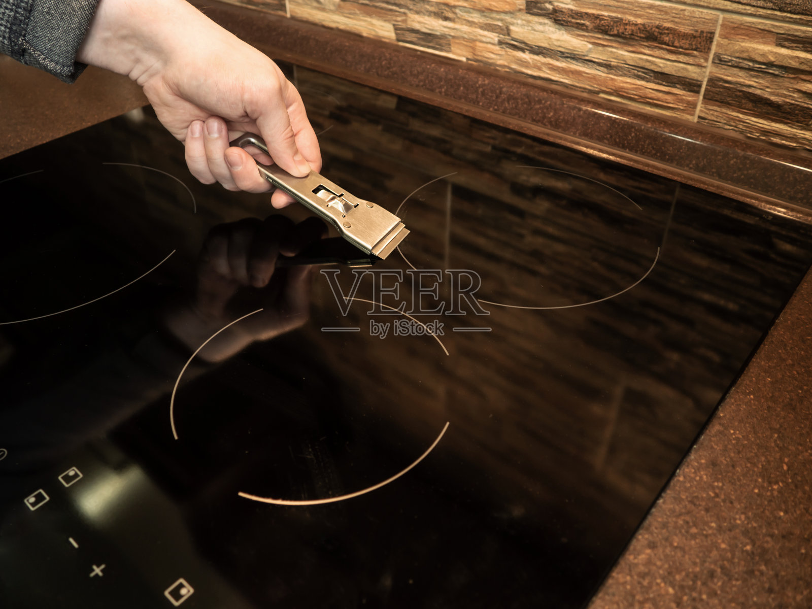 陶瓷表面内置感应或电滚刀。一名男子用刮板清洗电磁炉。肮脏的表面。烹饪板。照片摄影图片