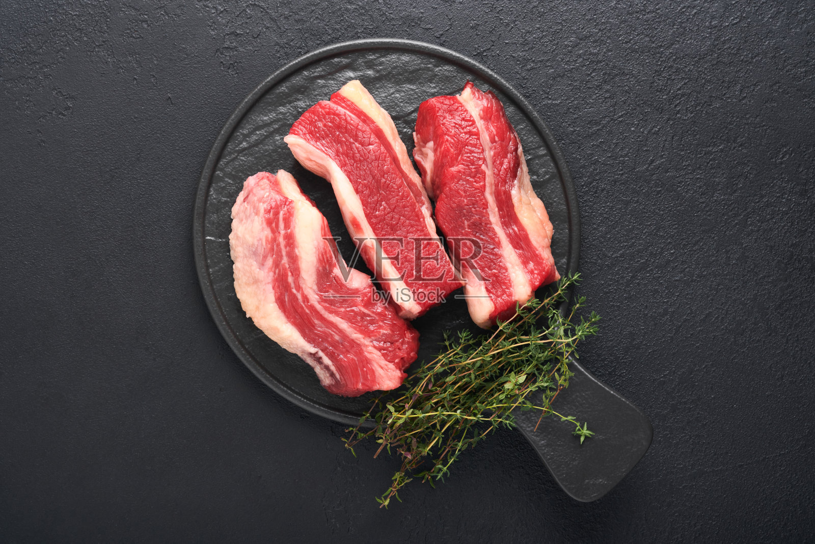 牛排牛肉。纽约生牛排加迷迭香和香料放在古老的铁板上，古老的深色石头背景。前视图。模拟。照片摄影图片