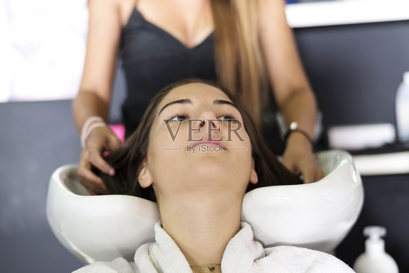 专业美发师在发廊为一位年轻美丽的女士洗头。照片摄影图片