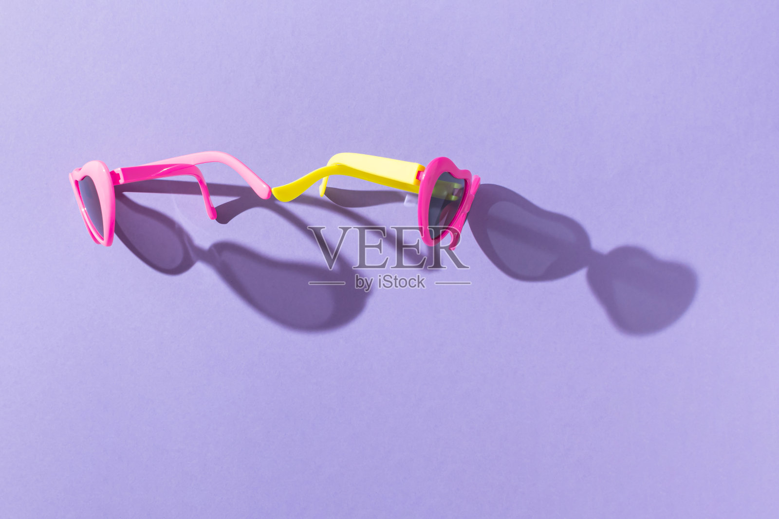 夏天的创意布局，彩色的心形太阳镜与阳光下的阴影在紫色的背景。最小的度假的概念。防晒的想法。新潮时尚眼镜。平的。照片摄影图片