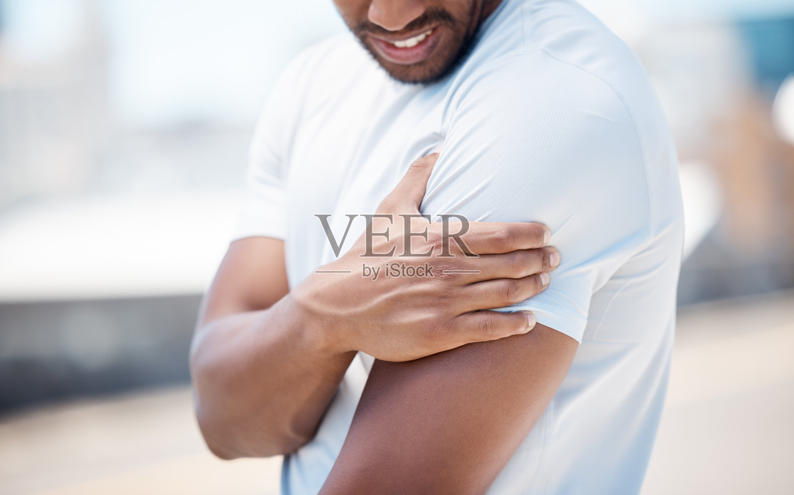 近距离观察一个男人在户外锻炼时，他的手臂和忍受肩膀疼痛。混合种族男性运动员在城市运动时因运动损伤感到不适照片摄影图片